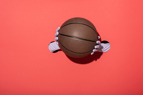 cropped view of woman in gloves holding basketball on red
