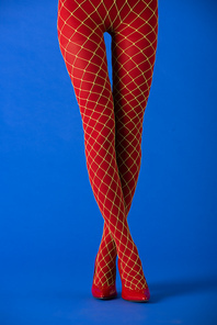 cropped view of model in fishnet tights and red heels standing with crossed legs on blue