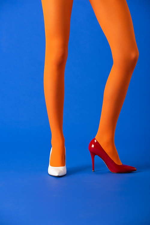 cropped view of model in orange tights, white and red heels posing on blue