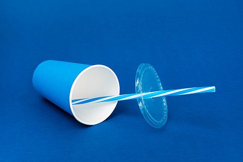 empty paper cup and plastic straw on blue background