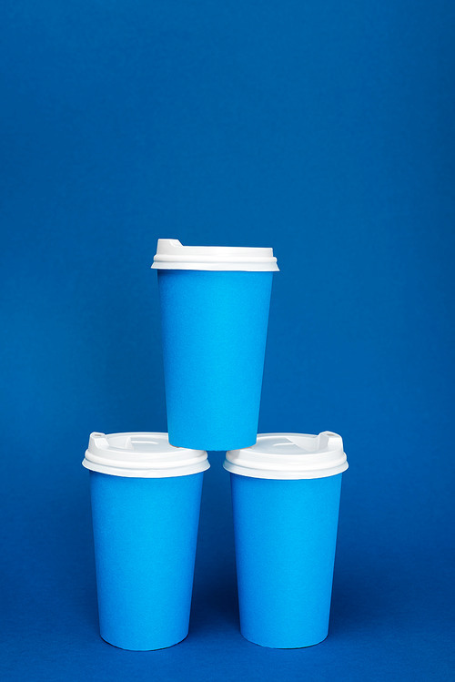 paper cups with coffee on blue background with copy space