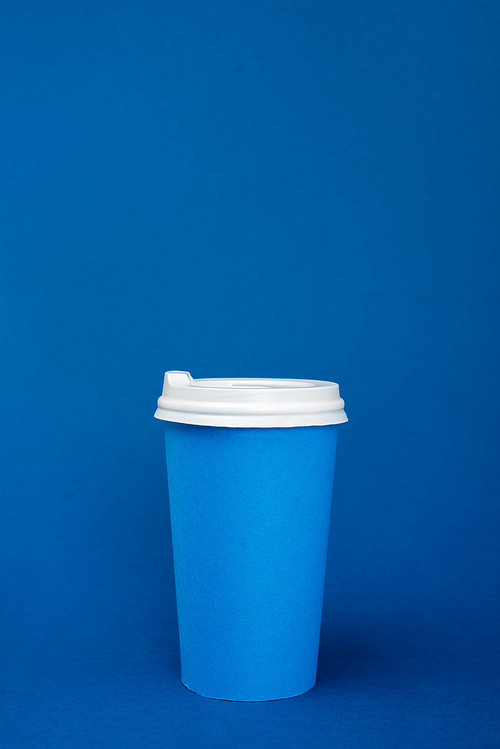 paper cup with coffee on blue background with copy space