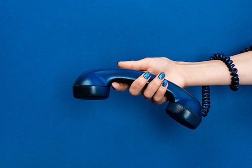 cropped view of woman holding handset on blue background
