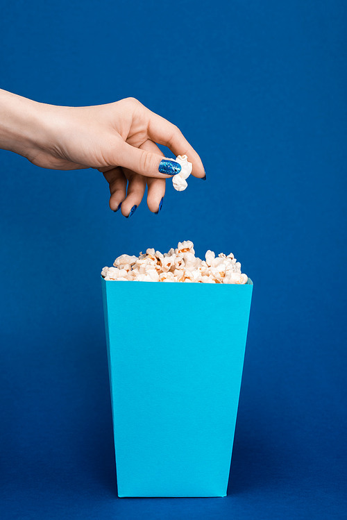 cropped view of woman holding popcorn on blue background