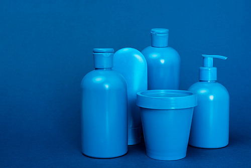 bottles with hair conditioner, shampoo, shower gel, liquid soap and bucket on blue background