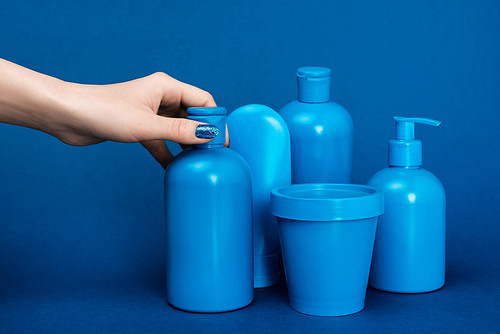 cropped view of woman holding bottle with shampoo on blue background
