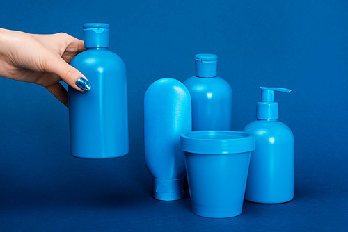 cropped view of woman holding bottle with shampoo on blue background