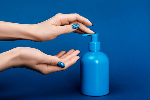 cropped view of woman pumping out liquid soap on blue background