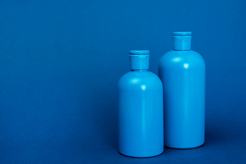plastic bottles with shampoo on blue background with copy space