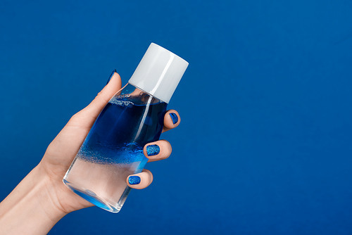 cropped view of woman holding micellar cleansing water isolated on blue