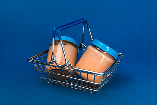 jars with baby food in shopping basket on blue background