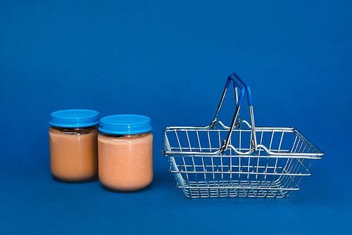 jars with baby food and shopping basket on blue background
