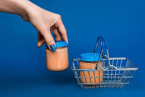 cropped view of woman putting in shopping basket jar with baby food on blue background