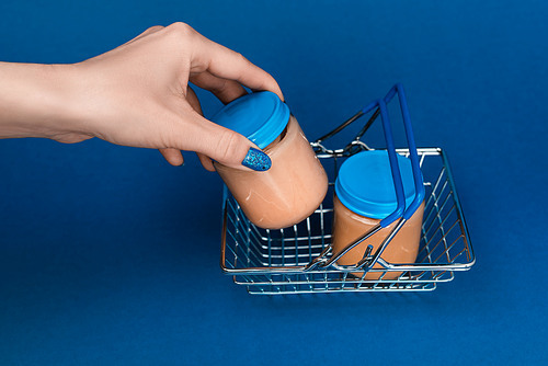 cropped view of woman putting in shopping basket jar with baby food on blue background
