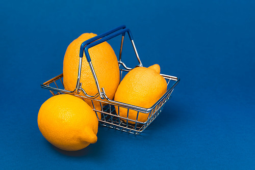 shopping basket with whole and organic lemons on blue background