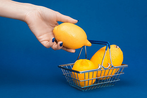 cropped view of woman putting lemon in shopping basket on blue background