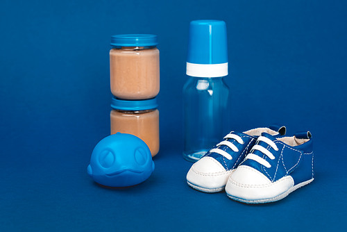 baby bottle, toy, baby shoes, jar with baby food ob blue background