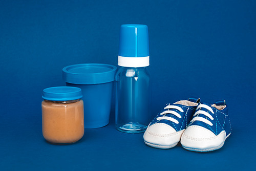bucket, baby bottle, baby shoes, jar with baby food ob blue background