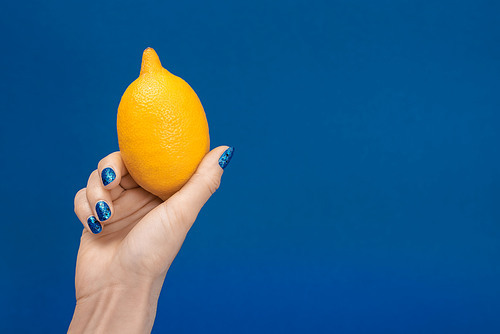 cropped view of woman holding whole lemon isolated on blue