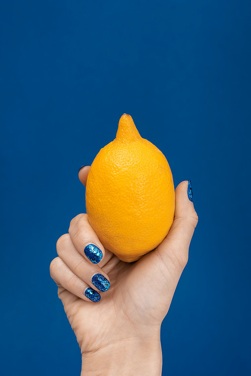 cropped view of woman holding whole lemon isolated on blue