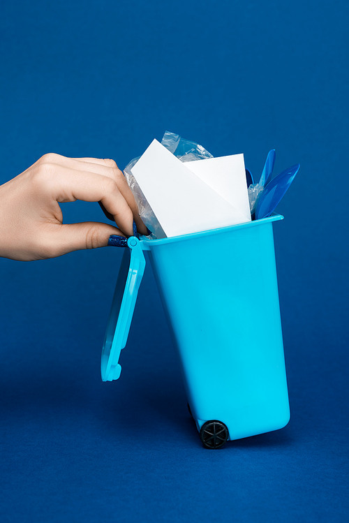 cropped view of woman holding toy trash can on blue background
