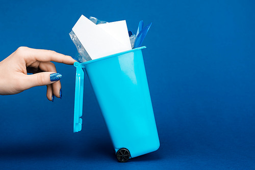 cropped view of woman touching toy trash can on blue background
