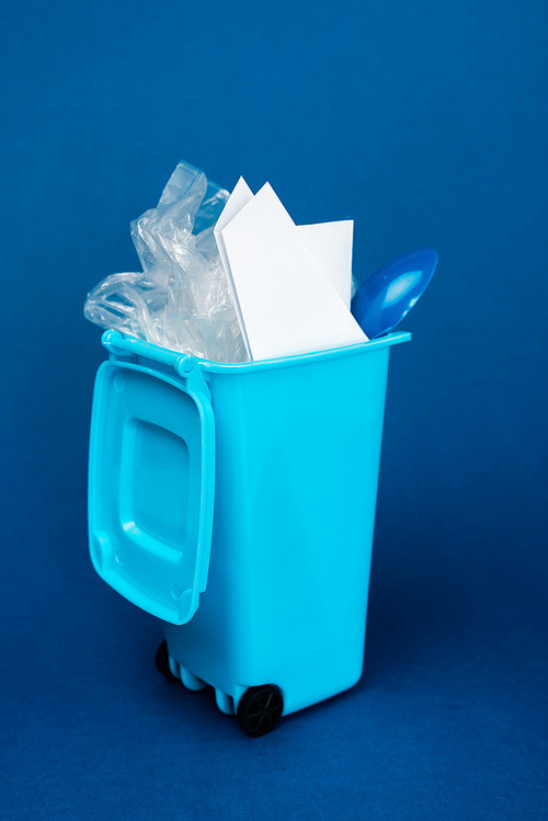 toy trash can with rubbish on blue background