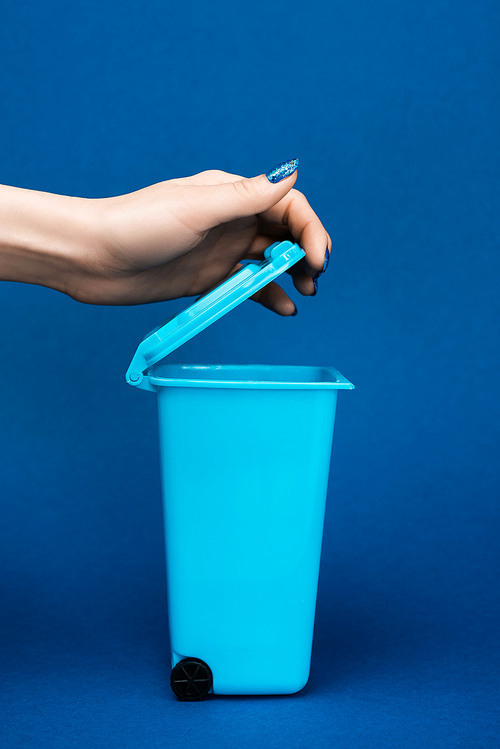 cropped view of woman opening toy trash can on blue background