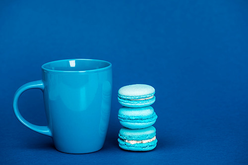 tasty french macaroons and cup on blue background with copy space