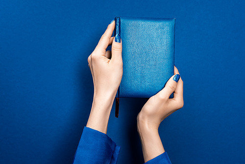 cropped view of woman holding notebook on blue background