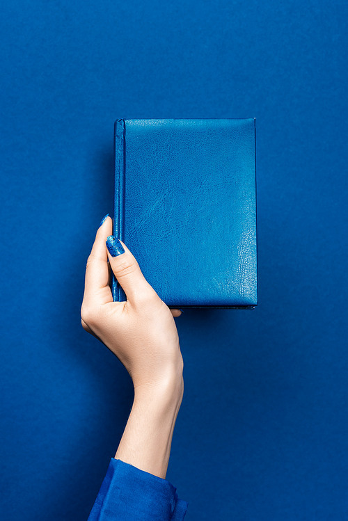 cropped view of woman holding notebook on blue background