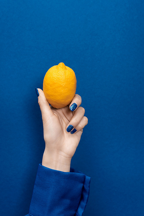 cropped view of woman holding lemon on blue background