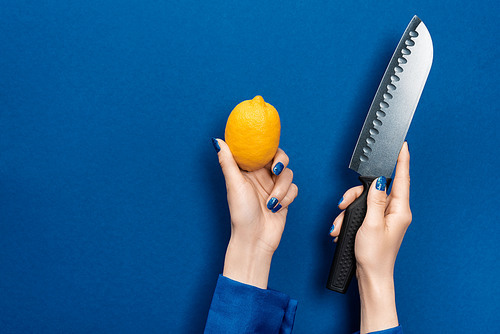 cropped view of woman holding lemon and knife on blue background