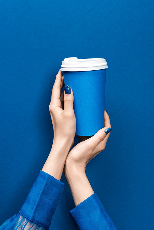 cropped view of woman holding paper cup on blue background