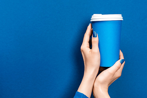 cropped view of woman holding paper cup on blue background