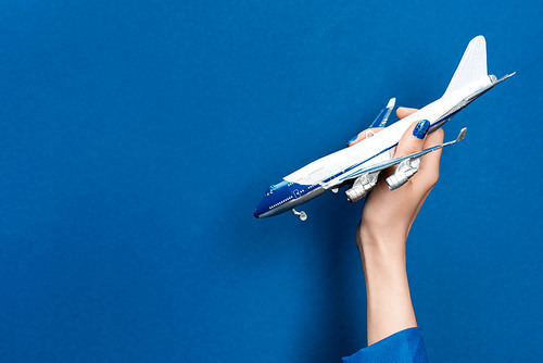 cropped view of woman holding model of plane on blue background