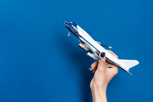cropped view of woman holding model of plane on blue background