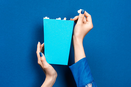cropped view of woman holding box with popcorn on blue background