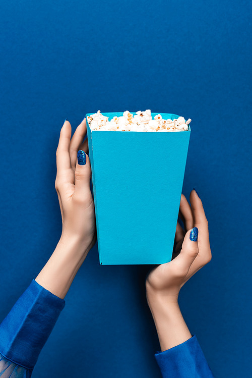 cropped view of woman holding box with popcorn on blue background