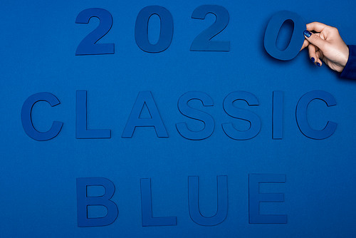 cropped view of woman holding number near classic blue lettering on blue background