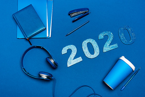 top view of notebooks, headphones, pens, stapler and 2020 numbers on blue background