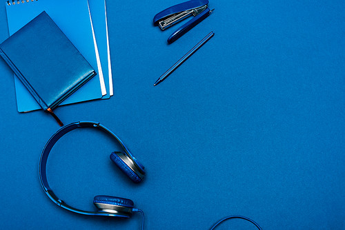 top view of notebooks, headphones, pen, stapler on blue background