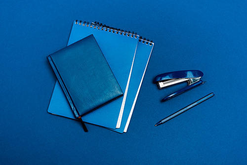 top view of notebooks, pen and stapler isolated on blue