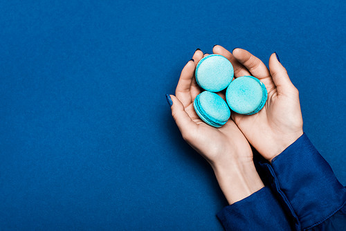 cropped view of woman holding french macaroons on blue background