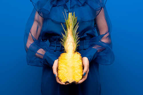 cropped view of woman holding cut pineapple on blue background
