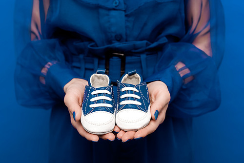 cropped view of woman holding baby shoes isolated on blue
