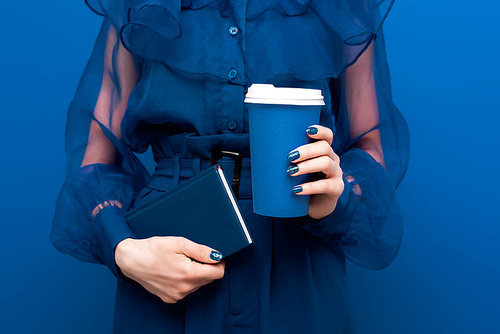cropped view of woman holding paper cup and notebook on blue background