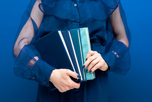 cropped view of woman holding books on blue background