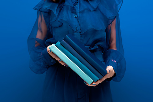 cropped view of woman holding books on blue background