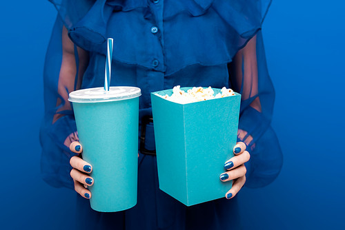 cropped view of woman holding popcorn and soda on blue background